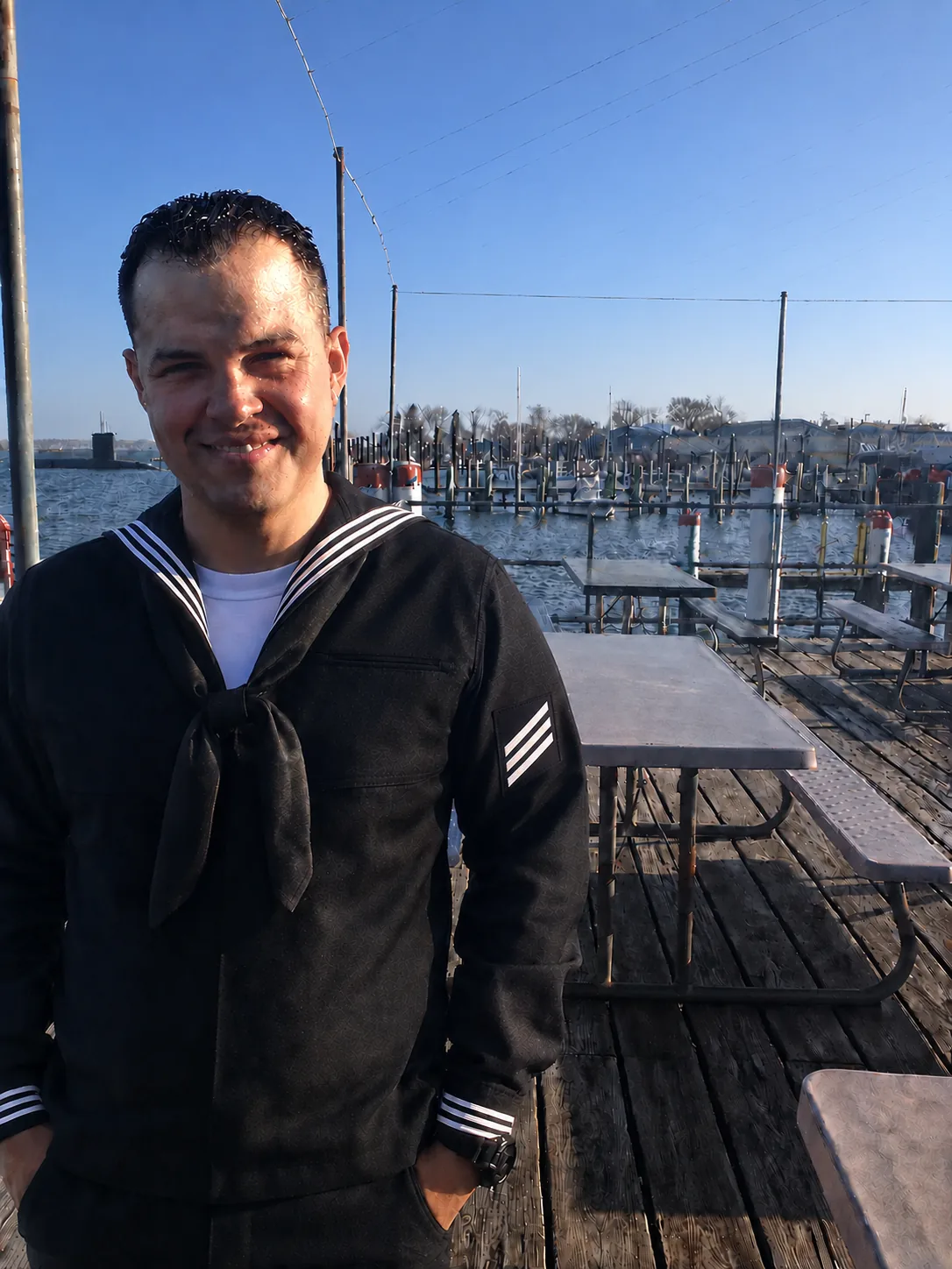A younger Josh Marx Dyer as an E-3 in Navy Service Dress Blues at a marina pier, before earning his submarine warfare qualification.